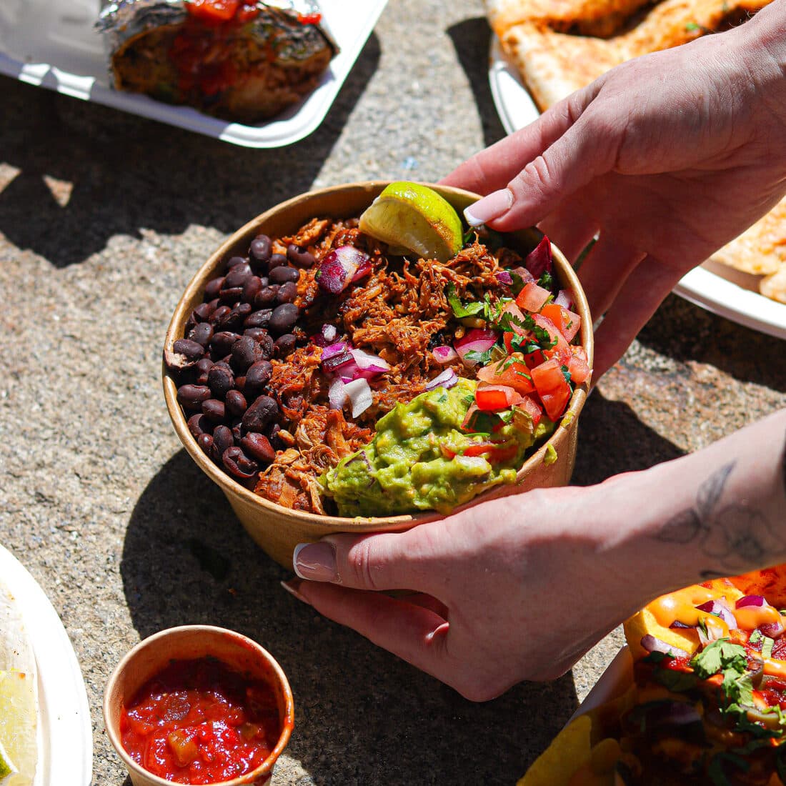 A loaded rice bowl held above a spread of tacos and quesadillas