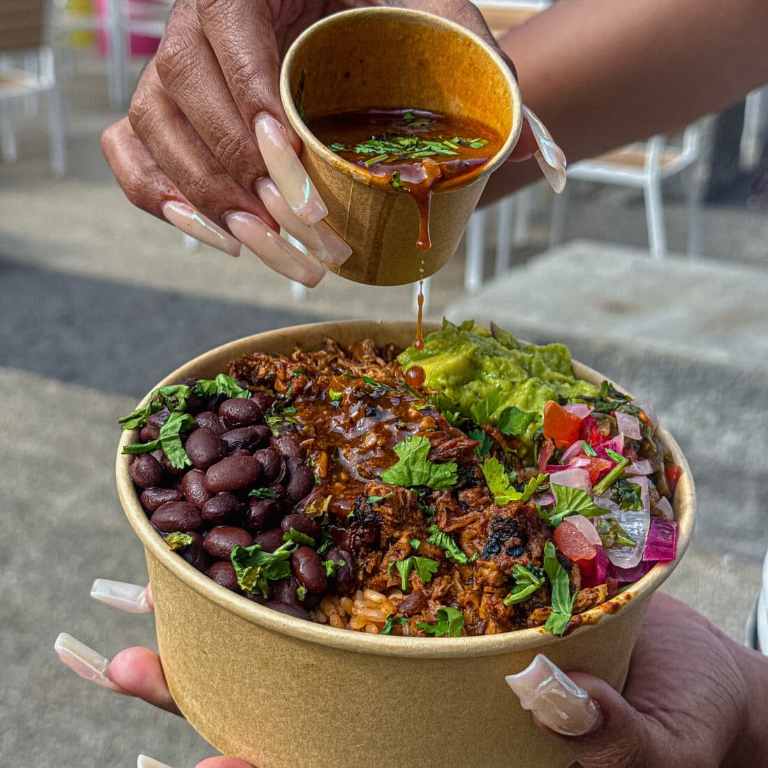 Rich birria consommé being poured over a loaded rice bowl