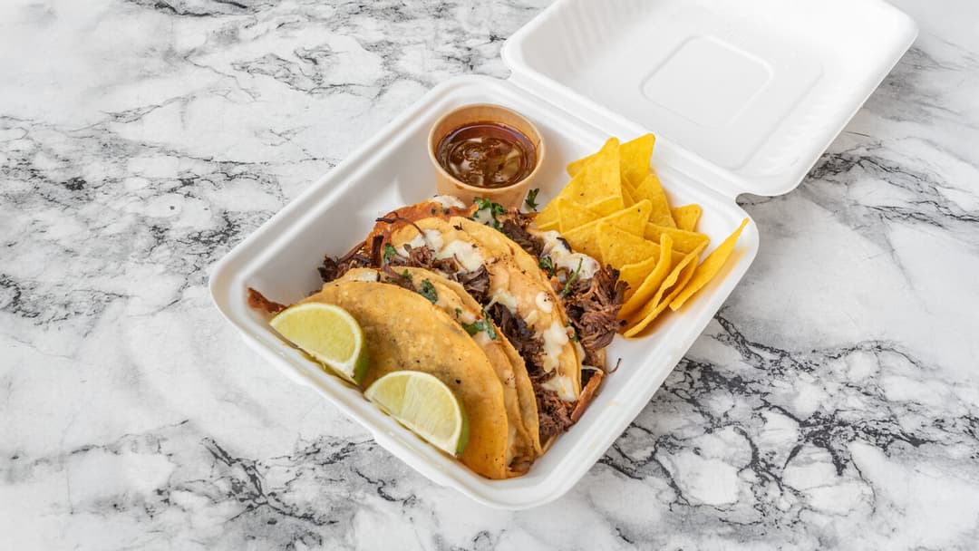 Three birria tacos with melted cheese, onion and coriander, served with nachos, lime and a pot of consommé